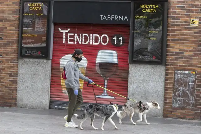 Un joven pasea a sus perros junto a un bar cerrado en Madrid, España. Foto Ap