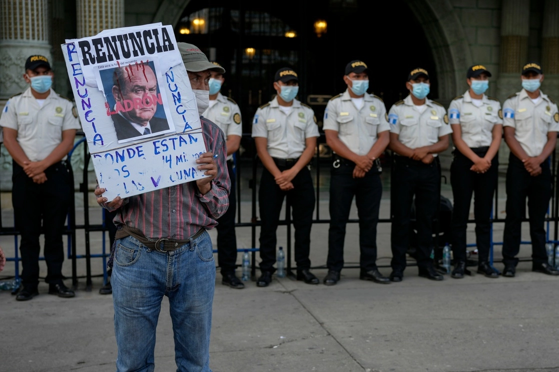 Un manifestante sostiene un cartel con un retrato del presidente guatemalteco Alejandro Giammattei frente al Palacio Nacional. Foto Ap 