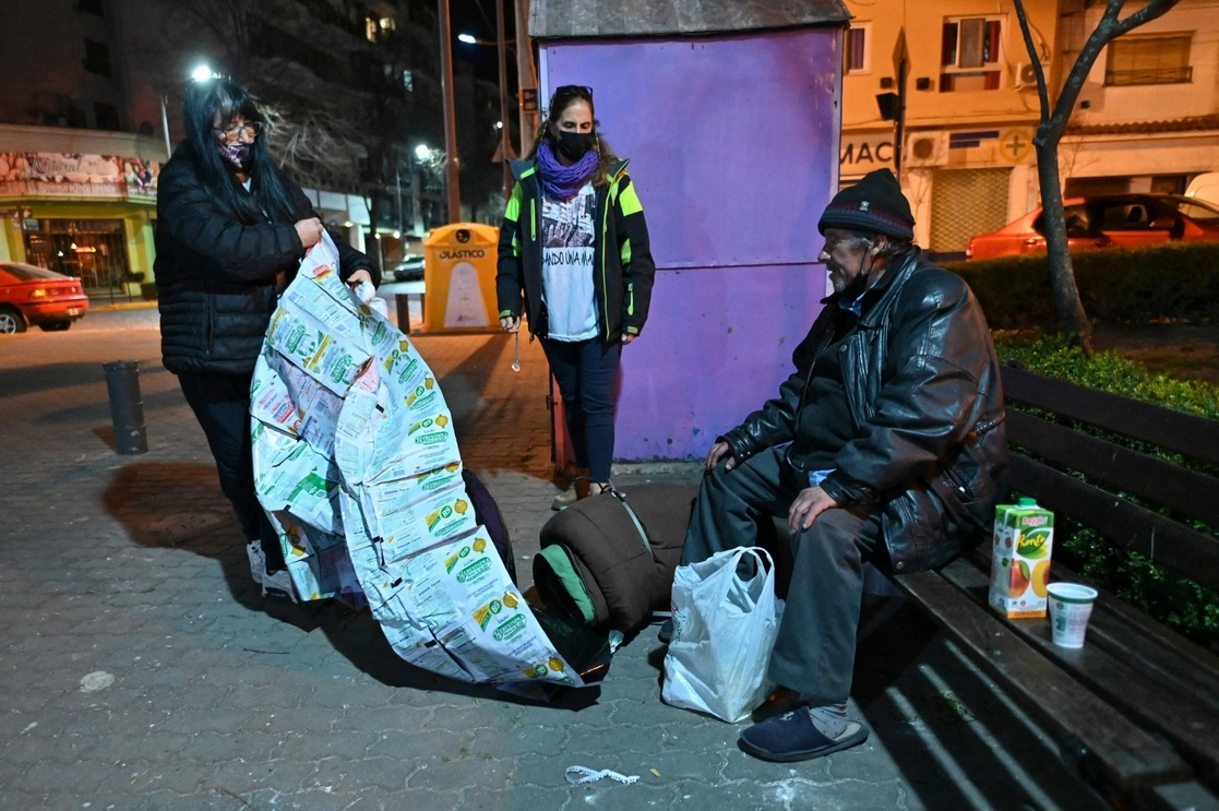 Integrantes de la ONG Dando una mano, entregan a un vagabundo comida y una frazada hecha con bolsas de leche recicladas en Buenos Aires. Foto Afp