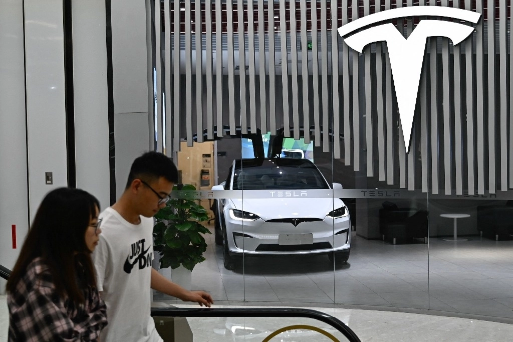 Personas pasan frente a una exposición de vehículos Tesla en la ciudad de Beijing, el 23 de julio de 2024. Foto Afp  