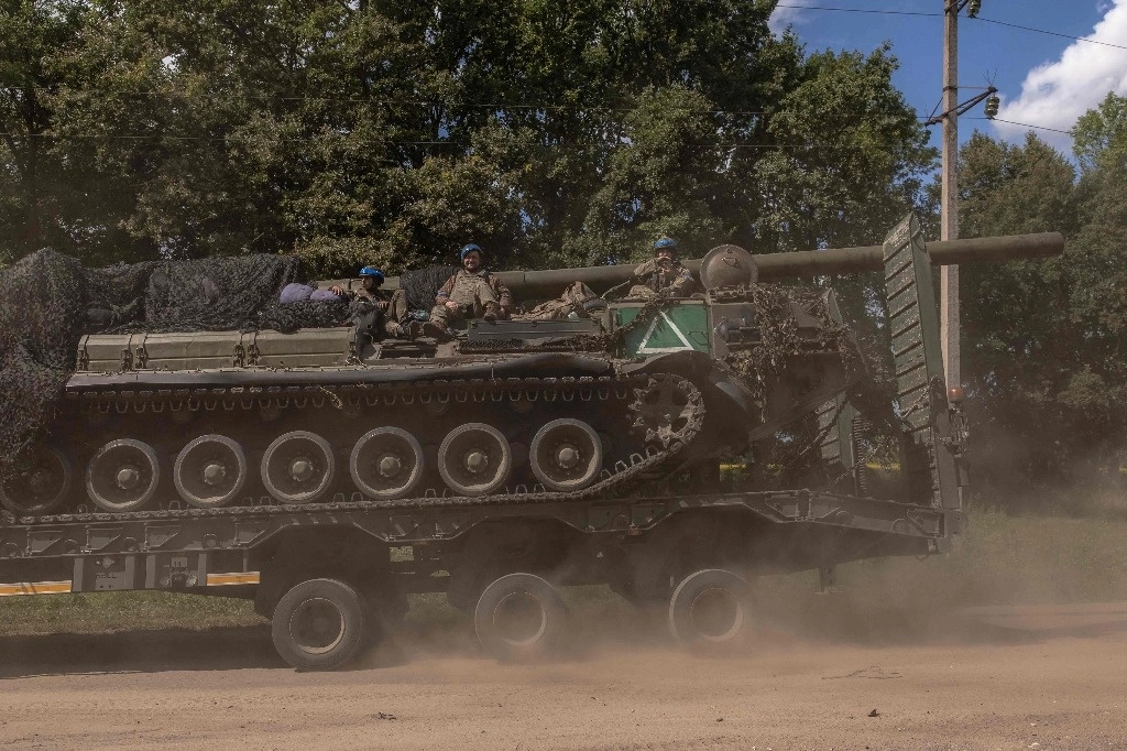 Militares ucranianos se sientan en un vehículo de artillería autopropulsado 2S7 Pion mientras es transportado por un camión militar, en la región de Sumy, cerca de la frontera con Rusia, el 11 de agosto de 2024, en medio de la invasión rusa de Ucrania. Foto Afp