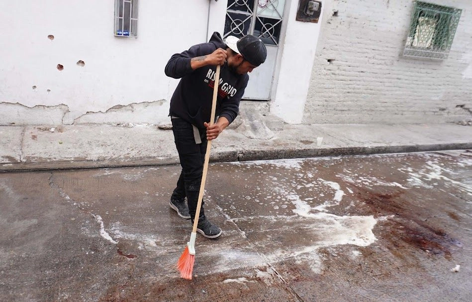 Un vecino de Barrio Nuevo, municipio de Irapuato, Guanajuato, limpia un área de la calle Bustamante, donde ayer se cometió un multihomicidio. Atrás de él, una pared con impactos de arma de fuego. Foto