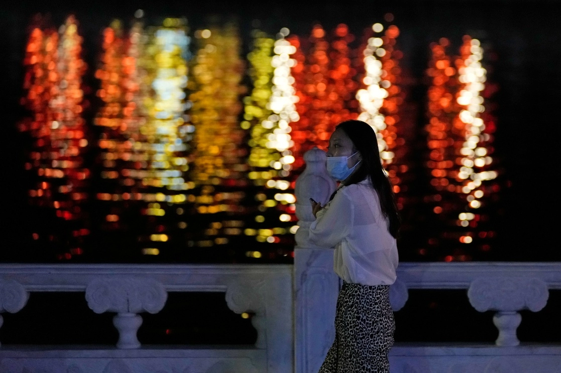 Una residente con cubrebocas pasa frente a las luces reflejadas en un río el 1 de mayo de 2022. foto Ap