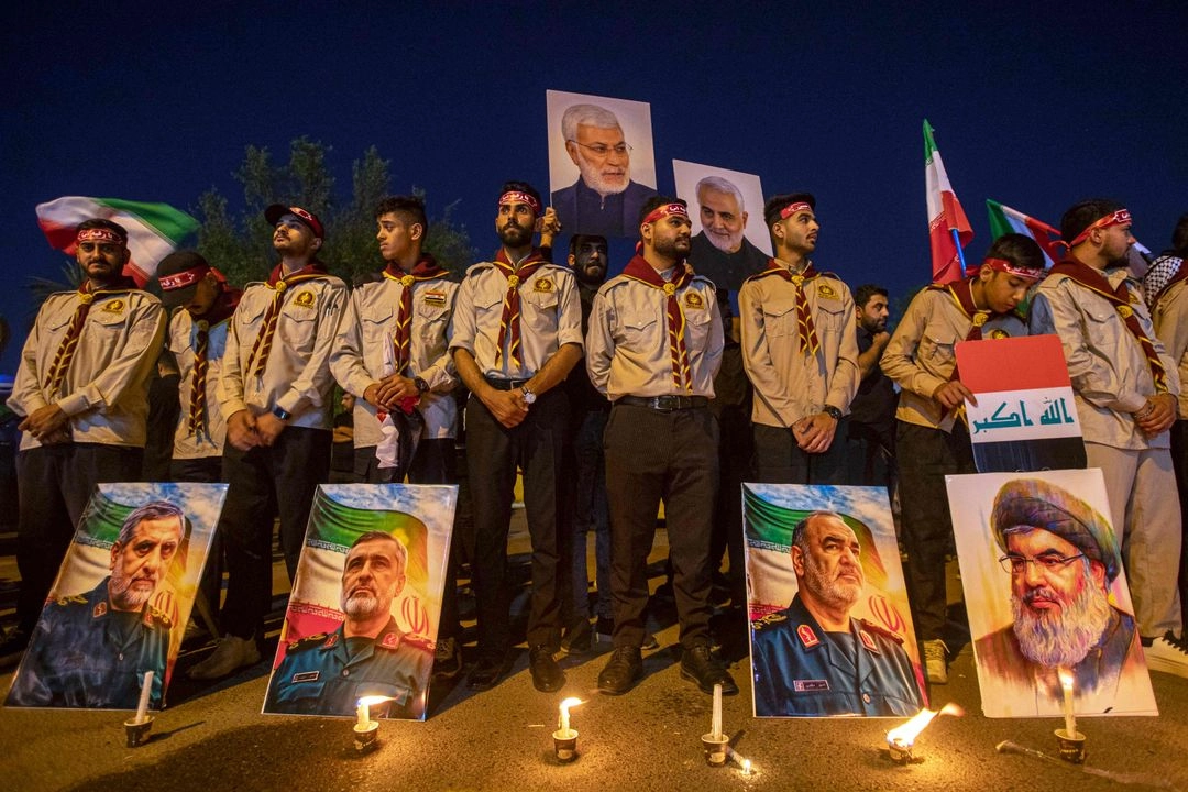 Frente a la embajada iraní en Bagdad, scouts hacen vigilia por miembros de la CGRI y científicos asesinados durante los ataques israelíes en Irán, cuyas fotos aparecen en primer plano.