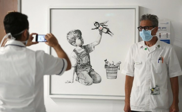 Personal sanitario toma fotografías frente a la nueva obra de Banksy, titulada 'Game Changer', que se exhibe en el Nivel C del Hospital General de Southampton. Foto AP 