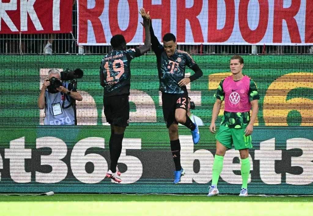 El centrocampista alemán del Bayern Munich #42 Jamal Musiala celebra el primer gol de su equipo con el defensor canadiense del Bayern Munich #19 Alphonso Davies (izq.) durante el partido de fútbol de la primera división alemana Bundesliga entre VfL Wolfsburg y FC Bayern Munich en Wolfsburg, norte de Alemania, el 25 de agosto de 2024. Foto Afp