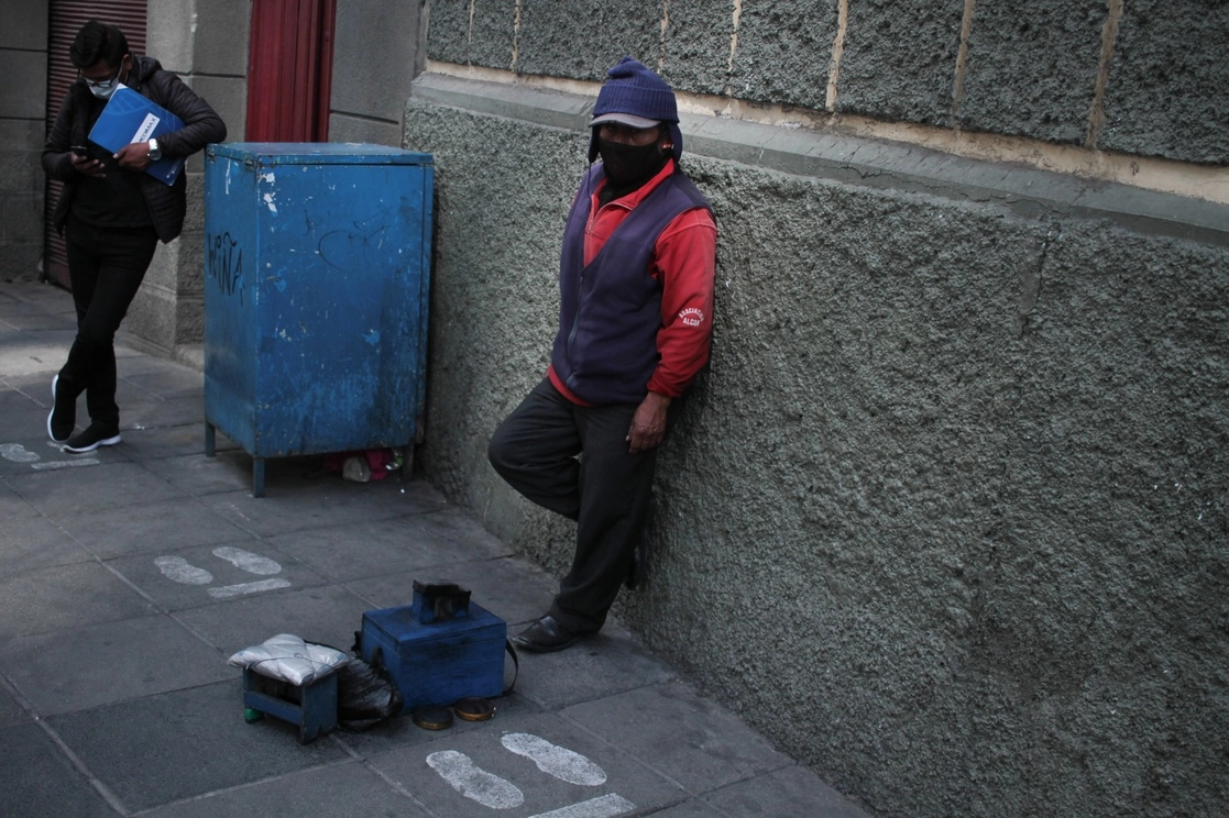  Un limpiador de calzado espera por clientes en una calle, en La Paz, Bolivia. Foto Xinhua