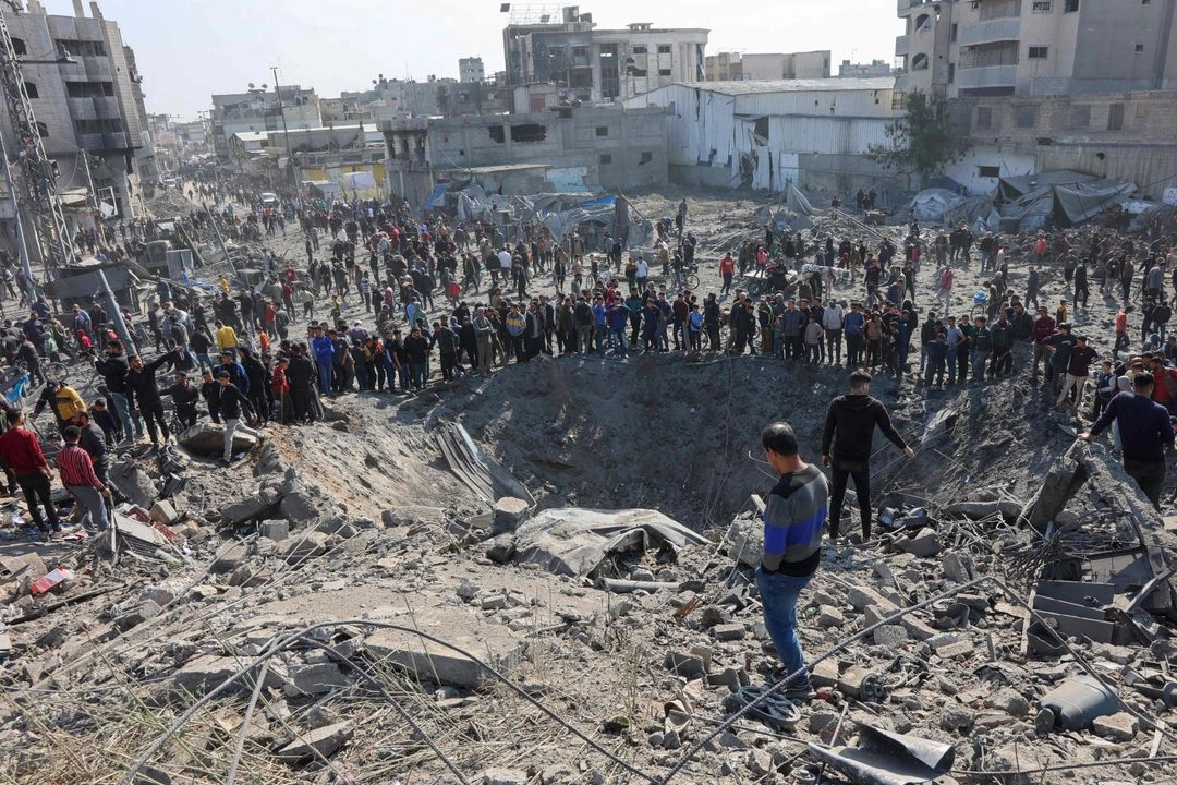 Palestinos se reúnen alrededor de un gran cráter luego de un ataque israelí contra un taller de metalistería en el barrio de Zaytoun en la ciudad de Gaza el 13 de abril de 2025.
