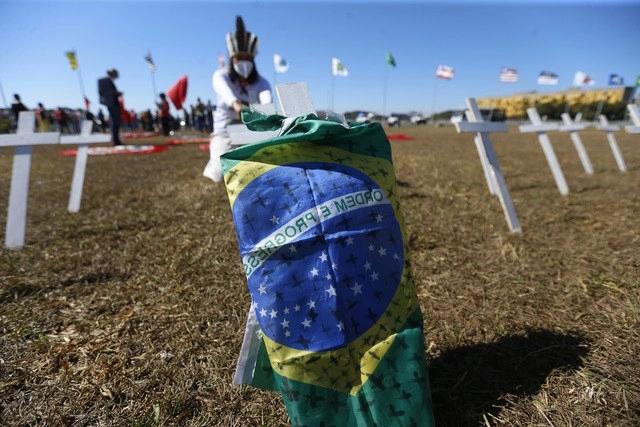 Una bandera de Brasil rodea una de cientos de cruces colocadas en memoria de los fallecidos por Covid-19. Foto Xinhua