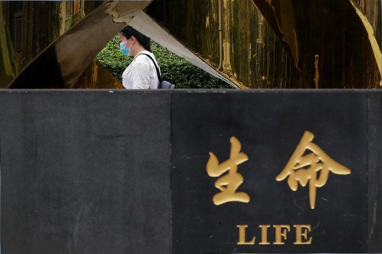 Una mujer con cubrebocas camina en un parque de Pekín, China. Foto Ap