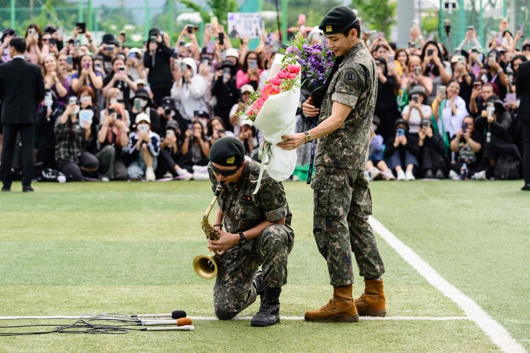 RM (izq.), miembro de la banda juvenil de K-pop BTS, toca el saxofón mientras V observa con ramos de flores en un centro deportivo al aire libre en Chuncheon, el 10 de junio de 2025, tras su liberación de 18 meses de servicio militar, en Corea del Sur. 