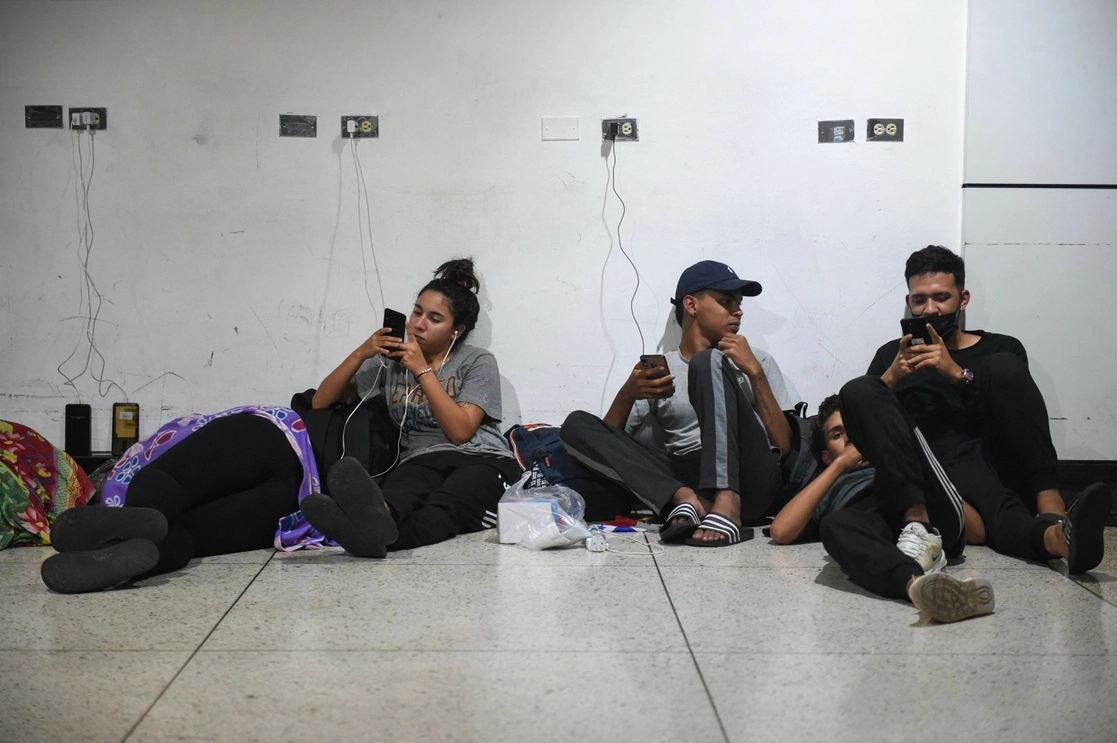 Venezolanos cargan sus teléfonos luego de su llegada desde México al Aeropuerto Internacional Simón Bolívar luego de no poder cruzar a EU. Foto AFP