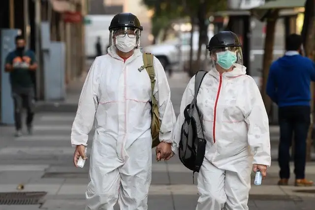 Personas portan trajes protectores mientras caminan por una calle de Santiago, capital de Chile. Foto Xinhua
