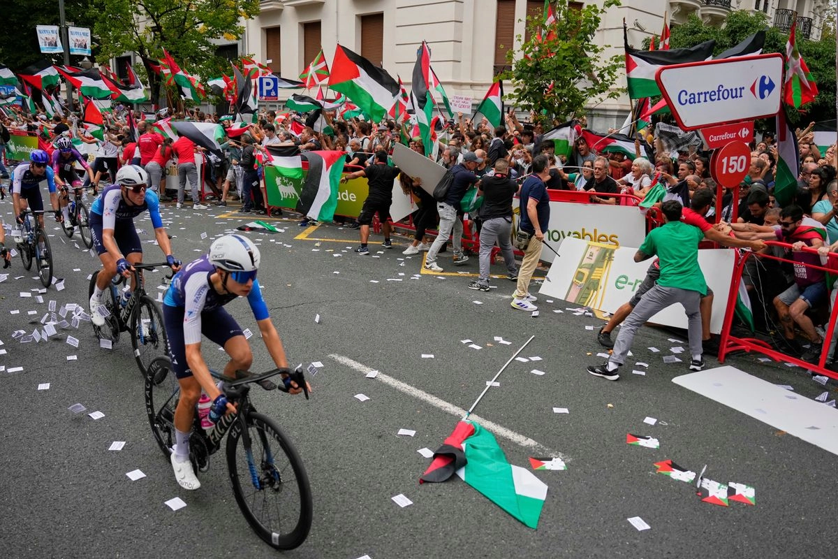 Los ciclistas del equipo Israel Premier Tech compiten mientras personas con banderas palestinas intentan interrumpir la undécima etapa de la carrera ciclista de la Vuelta a España, de Bilbao a Bilbao, España.