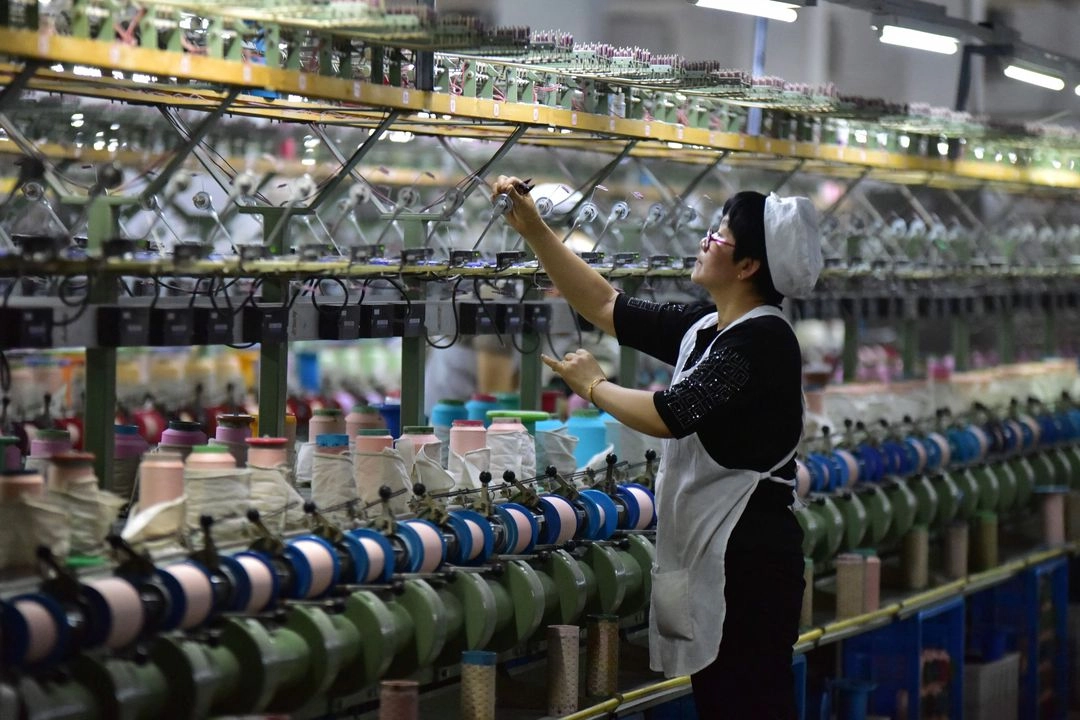 Un trabajador revisa una máquina en una fábrica que produce telas de seda en Fuyang, en la provincia oriental china de Anhui, el 16 de abril de 2025. Foto