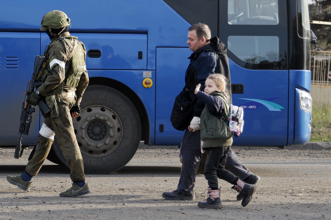 En Mariupol, un hombre y una niña que abandonan un refugio en una instalación acerera caminan escoltados por un soldado ruso. Foto Ap