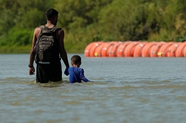 Migrantes pasan junto a grandes boyas que se utilizan como barrera fronteriza flotante en el Río Bravo. Foto Ap/ archivo