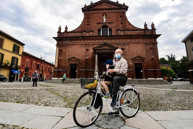 Los habitantes de Codogno, Italia, finalmente vuelven a pasear en bicicleta, todos con cubrebocas, tras el levantamiento del encierro. Foto Afp