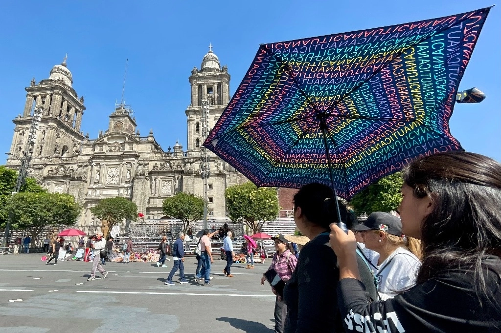 Paseantes en el Zócalo capitalino de la Ciudad de México se protegen del sol con una sombrilla. Foto Roberto García Ortiz / Archivo