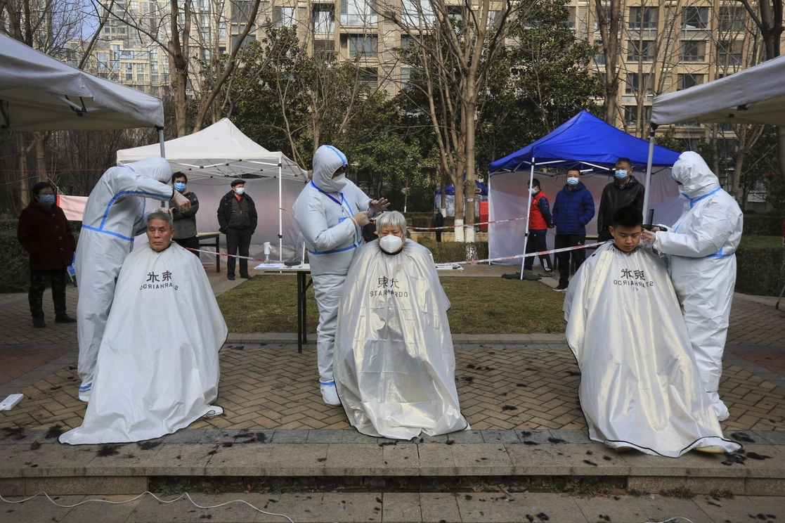 Estilistas cortan el cabello a tres clientes en una calle residencial en Xian, una de las ciudades china confinadas por los brotes de coronavirus, el 9 de enero de 2022. Foto Chinatopix vía Ap 