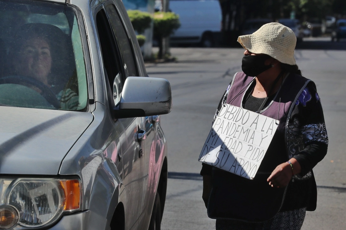 Una mujer pide a los automovilistas le ayuden con despensa o dinero ya que por la pandemia se quedó sin empleo. Foto Marco Pelaez / Archivo