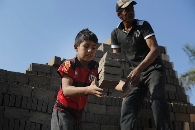 Con la ayuda de su hijo de 10 años, Hugo Godoy palea montículos de arcilla y tierra arenosa, preparándose para hacer los ladrillos del día siguiente, en Paraguay. Foto Ap