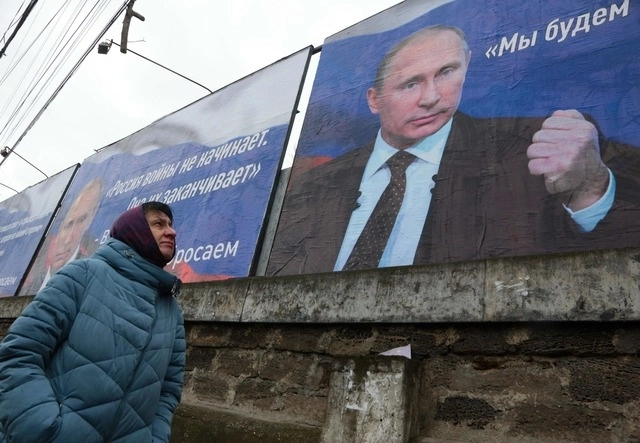 Una mujer pasa frente a enormes pancartas con imágenes del presidente ruso, Vladimir Putin, que dicen "Rusia no inicia las guerras, las termina" (izquierda) y "Apuntaremos a la desmilitarización y desnazificación de Ucrania" en Simferopol, Crimea. Foto Afp