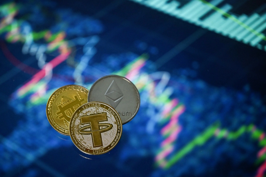 Las monedas Tether (USDT), Bitcoin y Etherium de recuerdo, chapadas en oro, dispuestas junto a una pantalla que muestra un gráfico de negociación, en una imagen tomada el 8 de mayo de 2022 en Londres, Inglaterra. Foto Afp