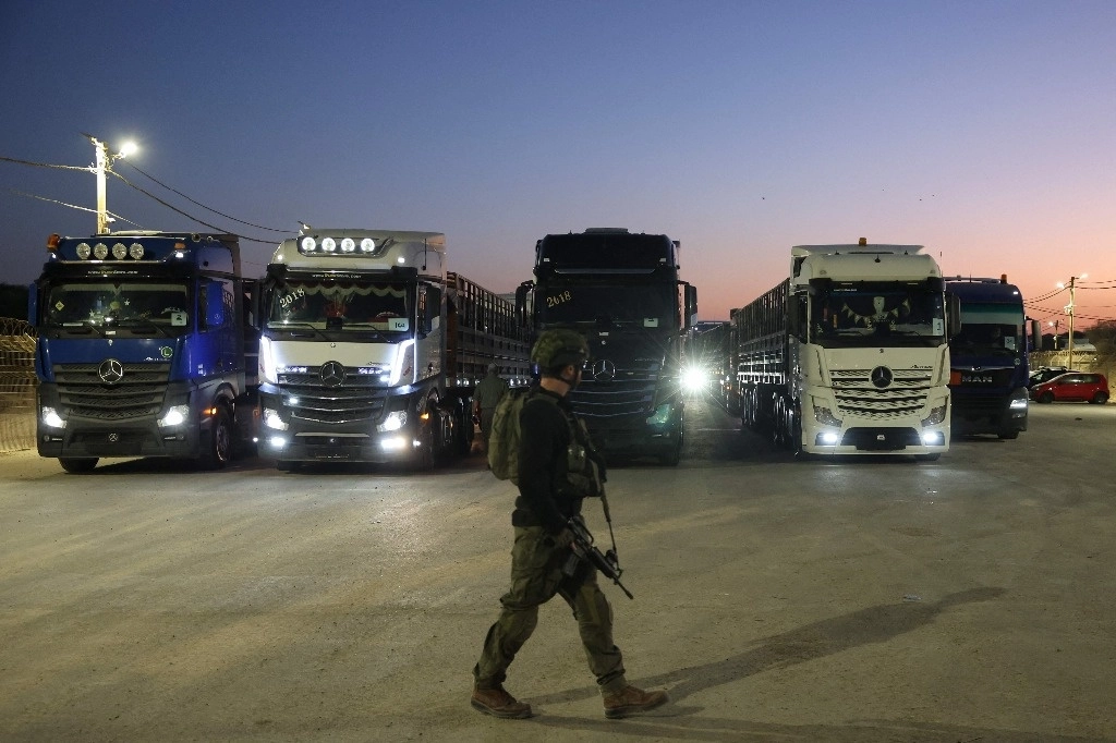 Soldado israelí camina frente a camiones cargados con ayuda humanitaria en la frontera entre Israel y la franja de Gaza, el 21 de octubre de 2024. Foto Afp 