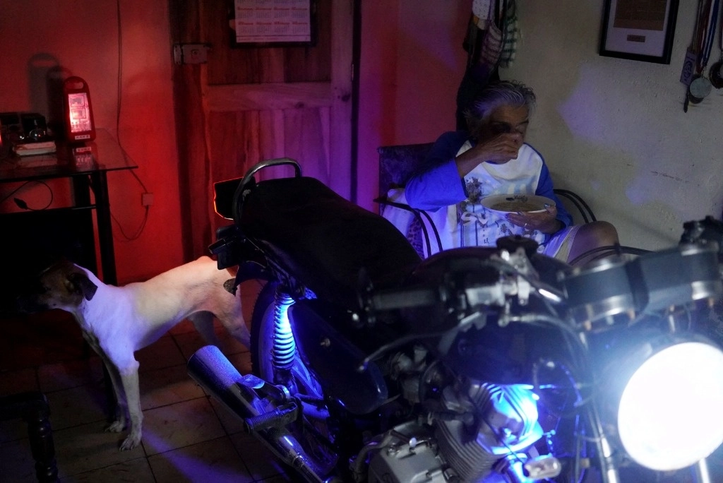 Una mujer come alumbrada por el faro de una moto en su casa en Matanzas, Cuba. Foto Afp