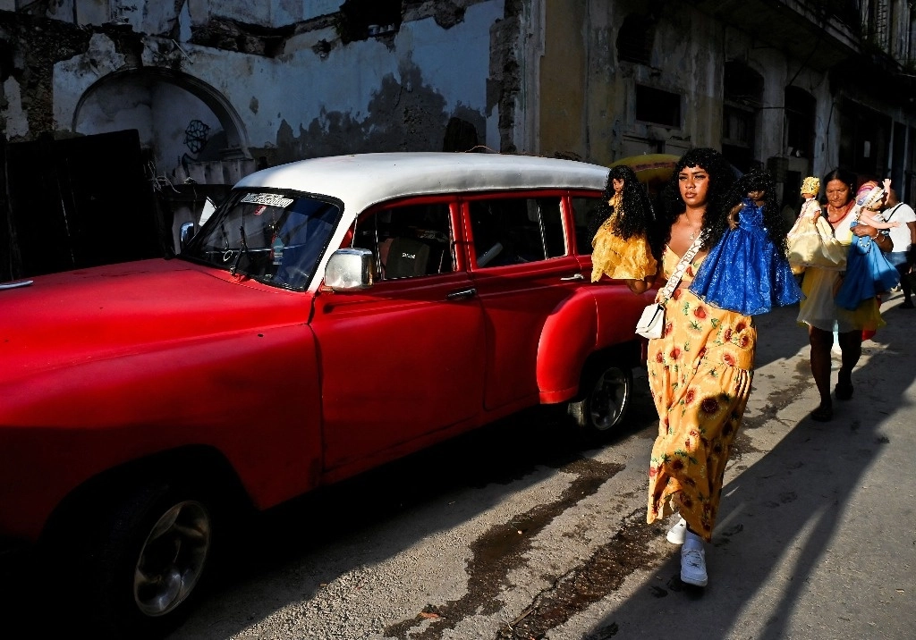 Mujeres caminan con dos muñecas que representan a la santa patrona de Cuba, Nuestra Señora de la Caridad del Cobre y la virgen de Regla, durante las celebraciones del Día de Oxun en La Habana, Cuba, el 8 de septiembre de 2024. Foto Afp