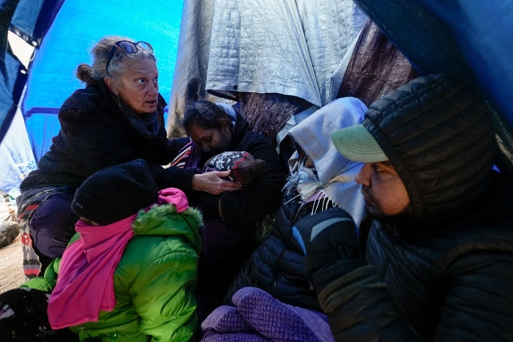 La voluntaria médica Karen Parker, izquierda, toca a un niño de 2 años con fiebre mientras habla con una familia de inmigrantes solicitantes de asilo mientras esperan ser procesados ​​en un campamento montañoso improvisado después de cruzar la frontera con México. 2 de febrero de 2024, cerca de Jacumba Hot Springs, California. Foto Ap