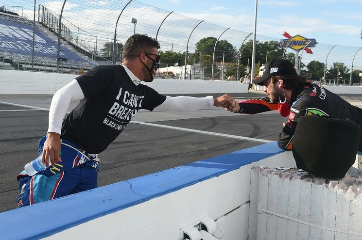 El piloto mexicano Daniel Suárez (derecha), saluda  a Bubba Wallace del auto #43, quien viste una playera en apoyo al movimiento de protesta por el caso de George Floyd; en la carrera disputada el 10 de junio en Martinsville, Virginia. Foto. Afp 