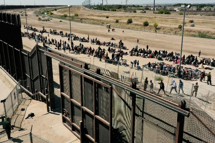 Migrantes esperan a lo largo del muro fronterizo para entregarse a los agentes de la Patrulla Fronteriza de EU para el procesamiento de solicitudes de inmigración y asilo después de cruzar el río Bravo hacia EU en la frontera con México, en El Paso, Texas, el 10 de mayop de 2023. Foto Afp