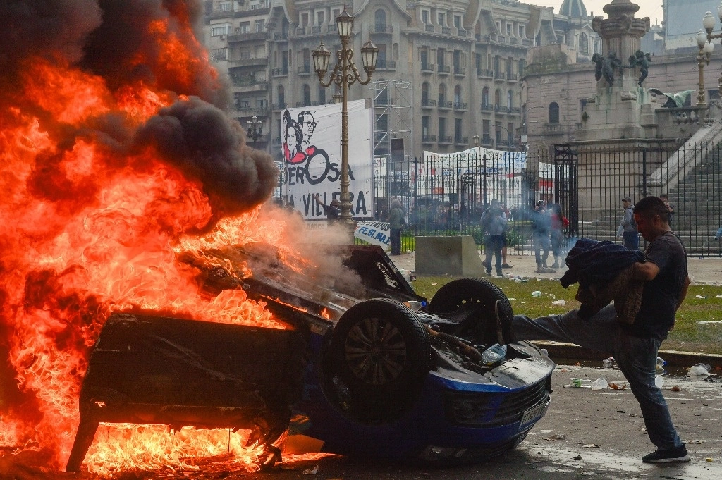 Un manifestante antigubernamental patea un vehículo en llamas durante enfrentamientos con la policía afuera del Congreso, donde los legisladores debaten un proyecto de ley de reforma promovido por el presidente argentino Javier Milei en Buenos Aires, Argentina, el miércoles 12 de junio de 2024. Foto Ap