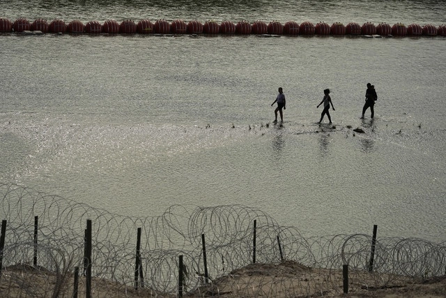 Migrantes pasan junto a grandes boyas que se utilizan como barrera fronteriza flotante en el Río Bravo. Foto Afp