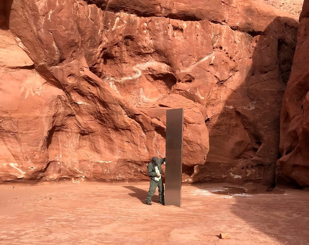 Un trabajador del estado de Utah observa un monolito de metal que se encontró instalado en el suelo en un área remota de roca roja en esta entidad estadunidense. La estructura alta y lisa fue encontrada durante una inspección en helicóptero del borrego cimarrón. Foto AP 