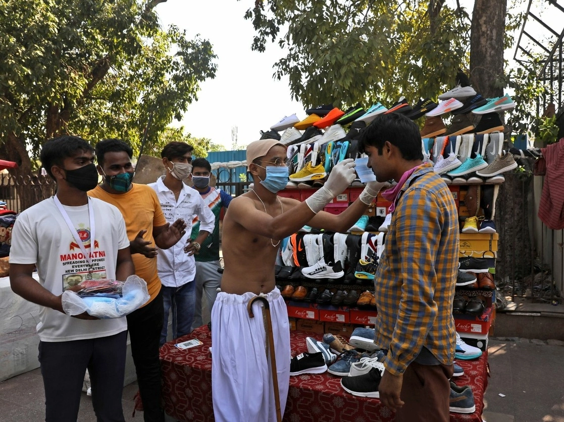 Un joven vestido como Mahatma Gandhi le pone un cubrebocas a un vendedor ambulante durante una campaña de concientización sobre Covid-19, en el aniversario del nacimiento del líder de la independencia, en Nueva Delhi, India. Foto AP Photo / Manish Swarup