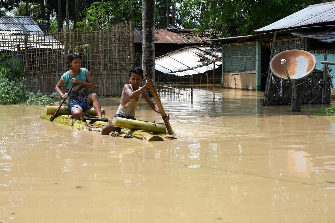 Niños se trasladan en una balsa de bambú tras las fuertes lluvias registradas en el distrito de Morigaon del estado indio de Assam, el 22 de mayo de 2022. Foto Afp