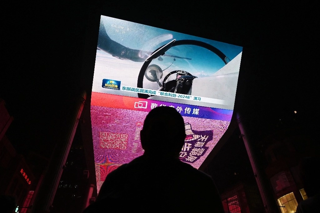 Un hombre mira un programa de noticias sobre ejercicios militares chinos en los alrededores de Taiwán, en una pantalla gigante frente a un centro comercial en Pekín, China, el 14 de octubre de 2024. Foto Afp