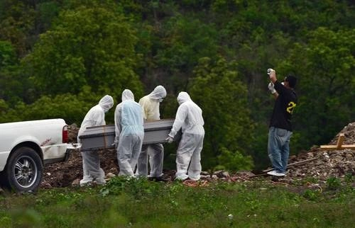 Un hombre graba con su celular el momento en que uno de sus familiares que falleció por Covid-19 está a punto de ser sepultado. Foto AFP 