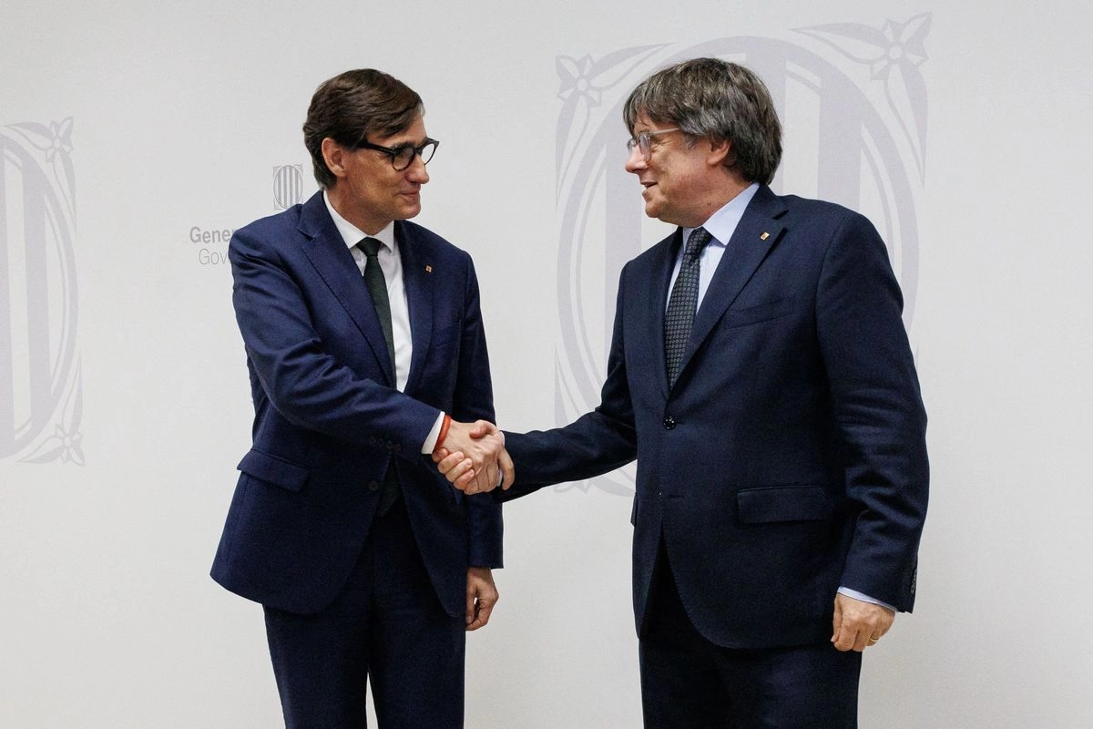 El presidente de Cataluña, Salvador Illa (izquierda), y el líder independentista catalán y eurodiputado Carles Puigdemont se dan la mano durante su reunión en la Delegación del Gobierno de Cataluña ante la Unión Europea en Bruselas, el 2 de septiembre de 2025. 