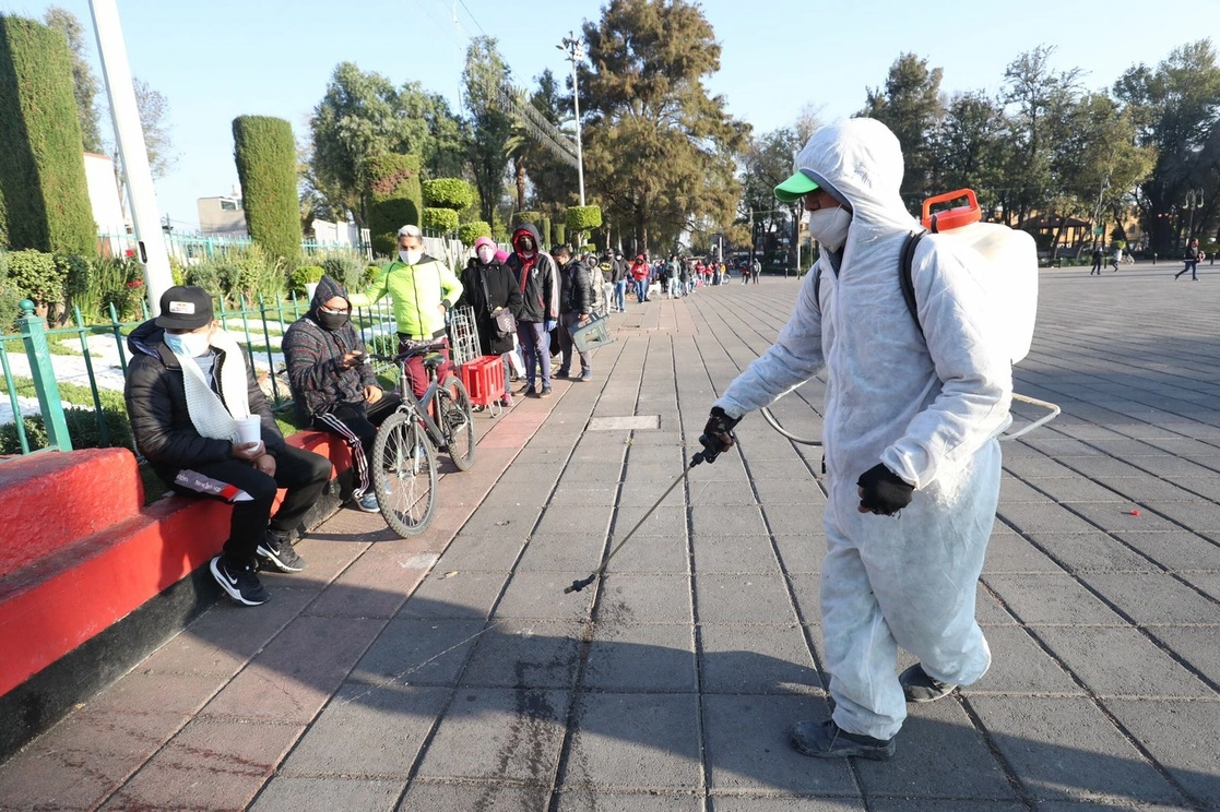 Personal de salud sanitiza la explanada de la alcaldía Xochimilco, donde decenas de personas realizan fila para acceder a una prueba PCR de detección de covid-19, en la Ciudad de México. Foto Luis Castillo