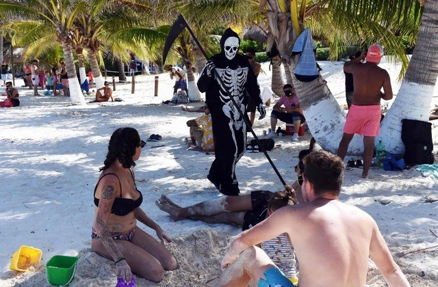 Una persona disfrazada de la muerte camina entre jóvenes en la playa de Puerto Morelos, Quintana Roo. Foto Afp 