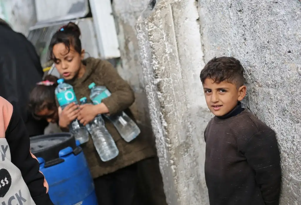 Niños esperan recibir agua en Rafá, en la franja de Gaza. Foto Xinhua 