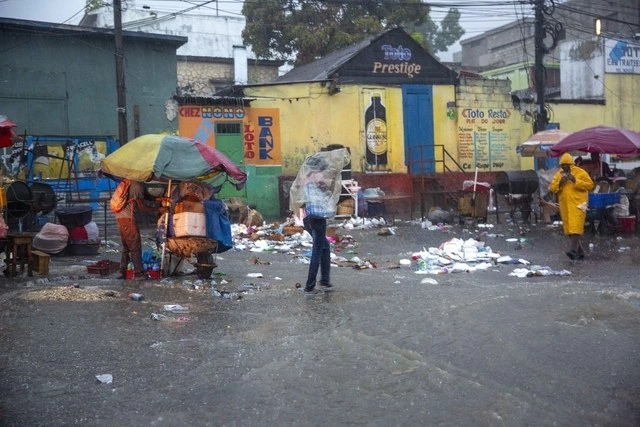Transeúntes se protegen de la lluvia en una calle de Puerto Príncipe, Haití, al paso de la tormenta tropical ' Laura'. Foto Ap