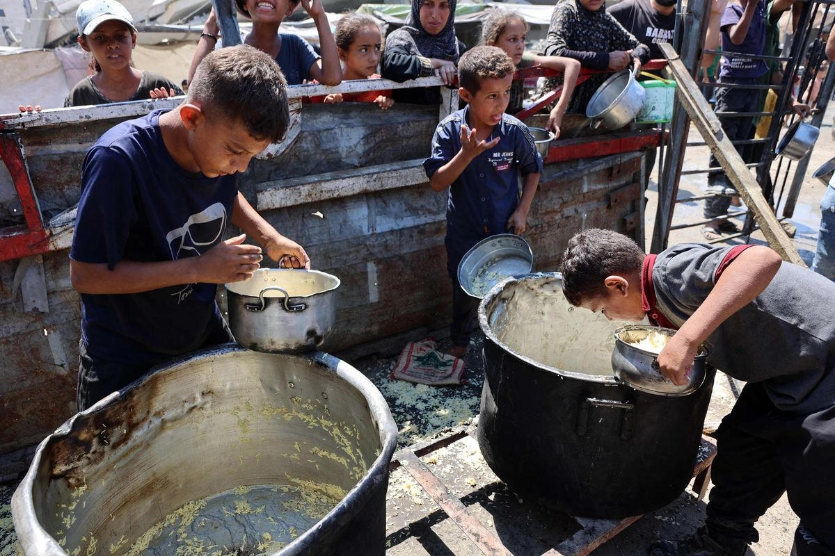 Niños palestinos raspan el fondo de ollas grandes para sacar el resto del arroz cocido, tras una distribución en un comedor social en la ciudad de Gaza, el 23 de agosto de 2025. Foto 