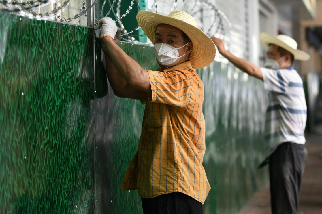 Trabajadores instalan barreras para asilar un área donde se detectó un brote de covid-19 en Nanchang, en la provincia central de Jiangxi, China. Foto Afp