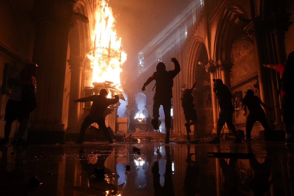Una iglesia consumida por el fuego y otra dañada, fue el resultado de ataques perpetrados por encapuchados durante una multitudinaria manifestación en la capital chilena. Foto Ap