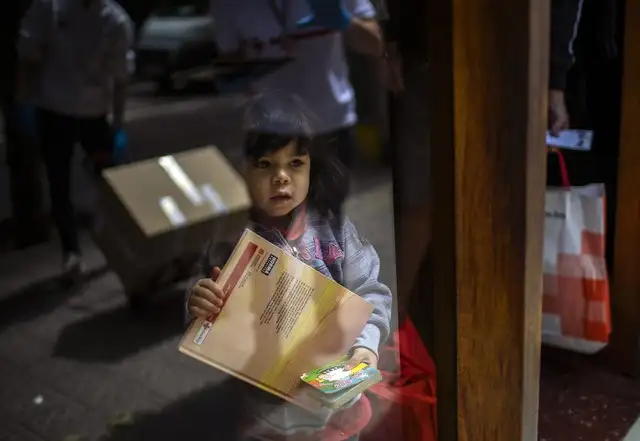 Una niña de tres años sostiene un libro infantil mientras su padre recibe una donación de comida de una ONG en su casa en Barcelona, España. Foto Ap
